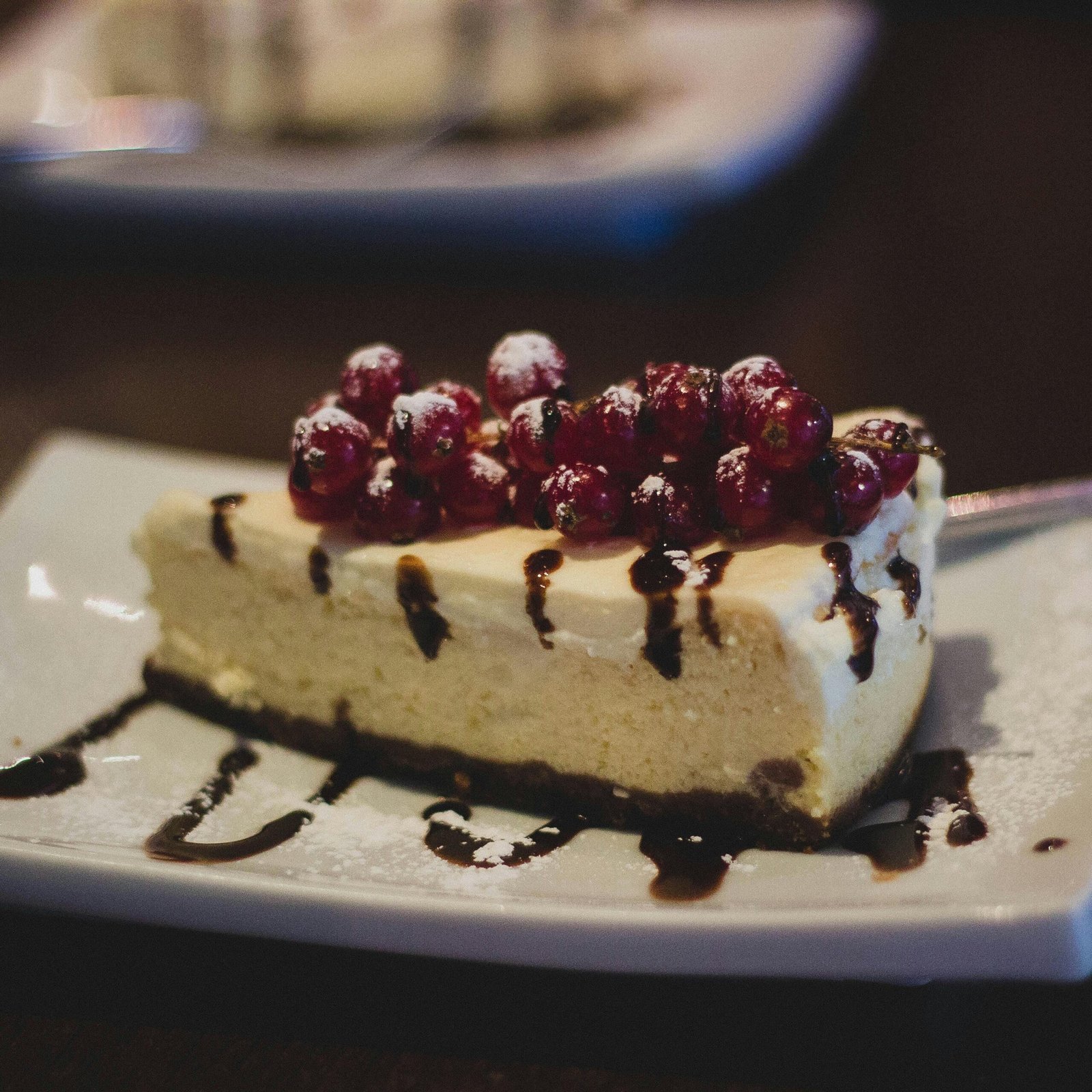 Slice of cheesecake topped with berries and chocolate drizzle on a plate.