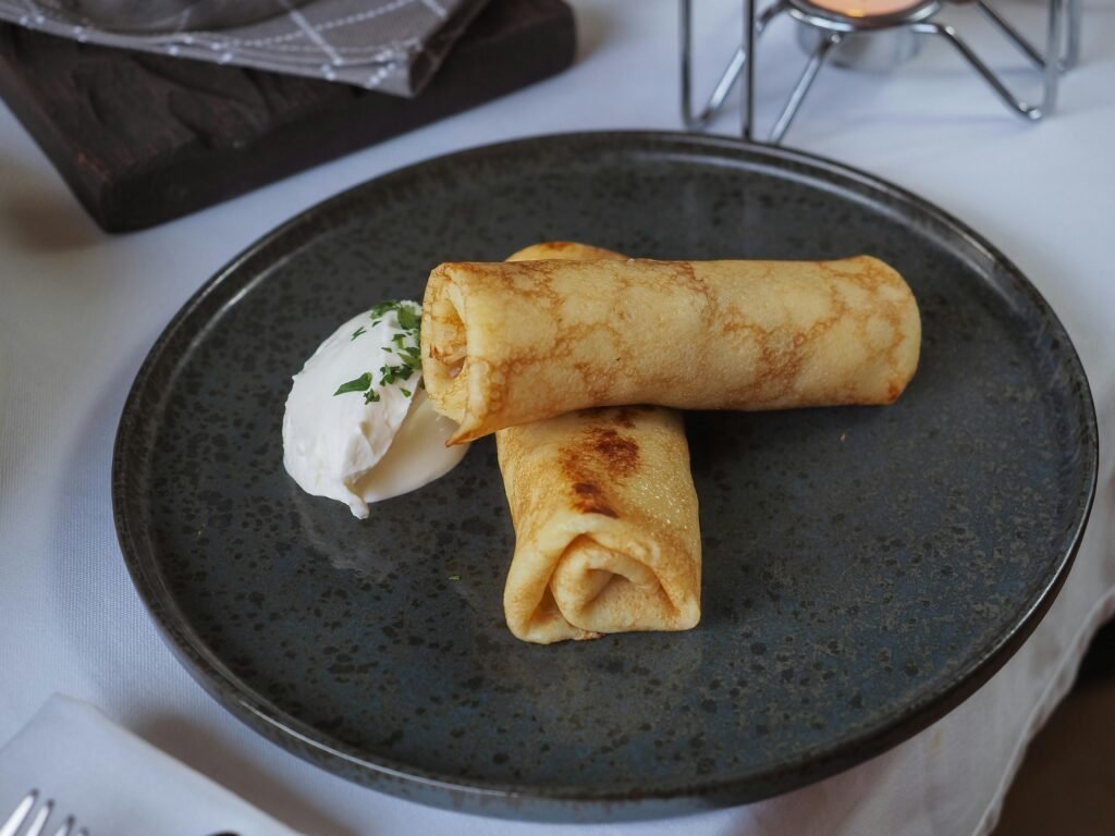 Savoury rolled crepes with a fresh cream dollop on a rustic plate.