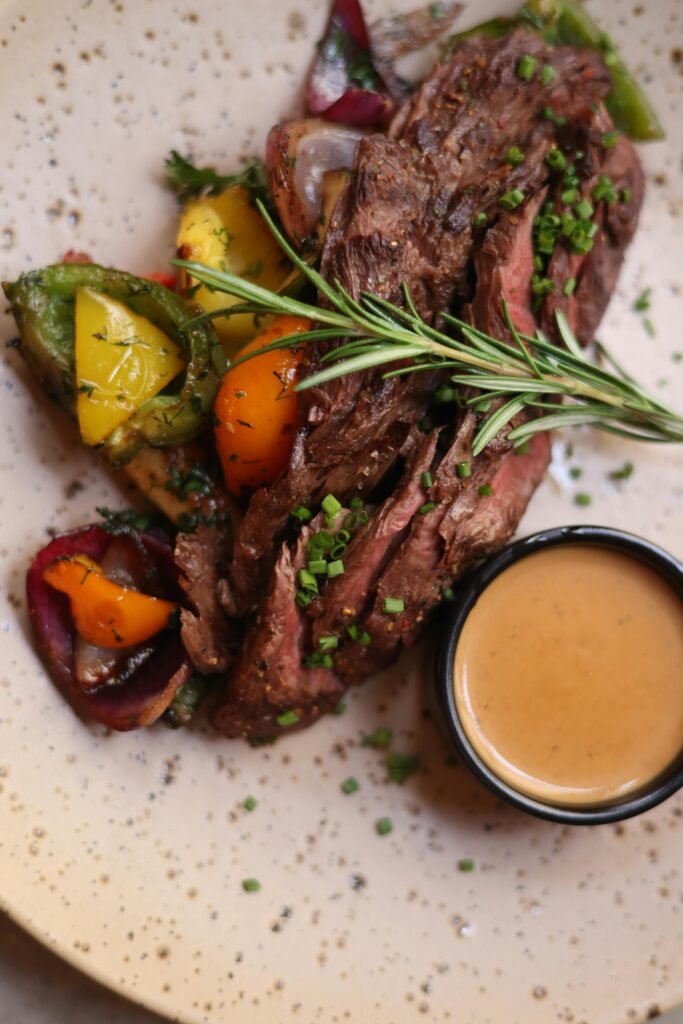 Delicious roasted lamb topped with chives beside grilled vegetables and a serving of gravy.
