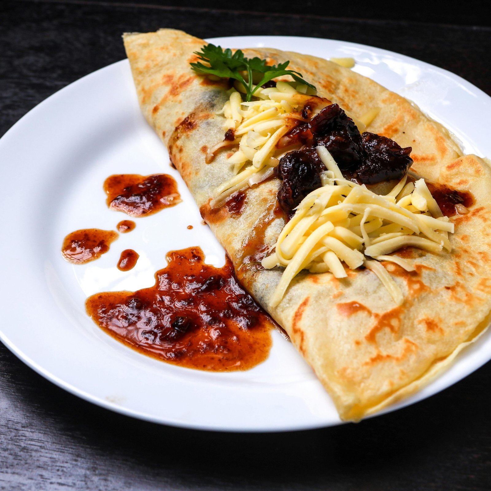 A mouthwatering crepe topped with melted cheese and fruit jam, displayed on a white plate.