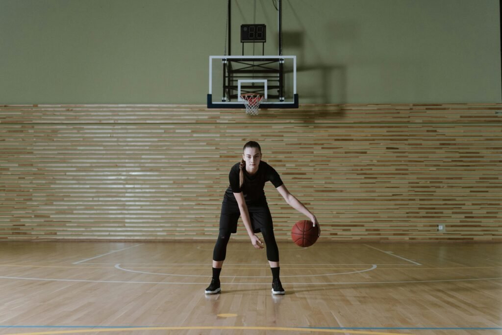 Focused young woman dribbling basketball in indoor court, embodying determination and athleticism.