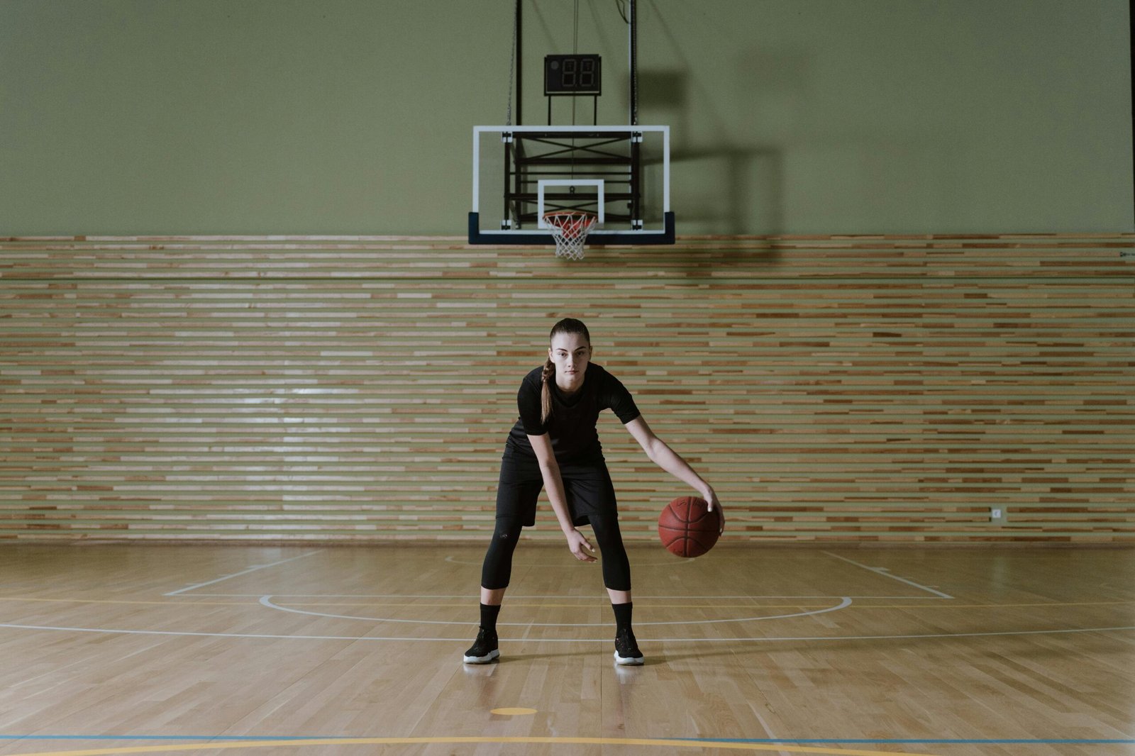 Focused young woman dribbling basketball in indoor court, embodying determination and athleticism.
