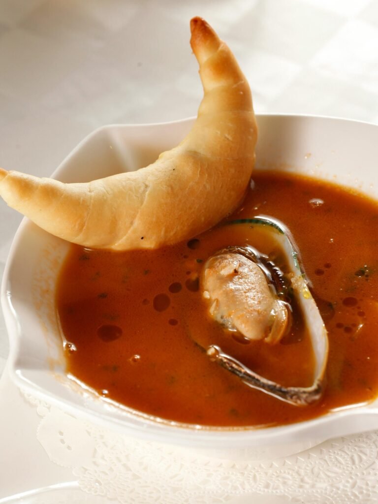 A savory tomato soup served with a crescent roll, perfect for a hearty meal.