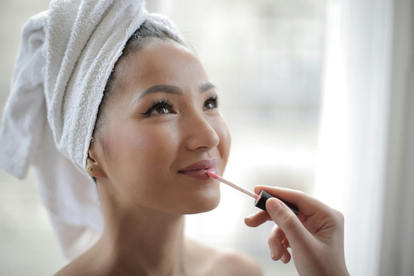 Young woman indoors enjoying skincare routine while applying lip gloss.