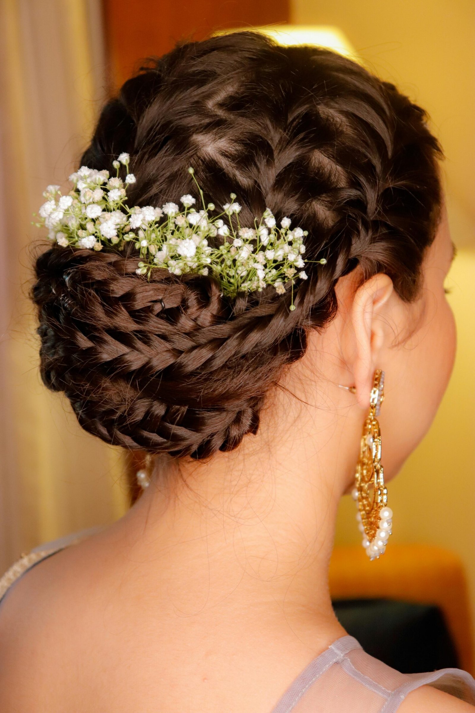 Close-up of a woman's braided bridal hairstyle adorned with delicate flowers and gold earrings.