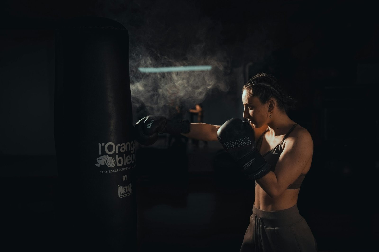A determined female boxer honing her skills by punching a bag in a dimly lit gym setting.