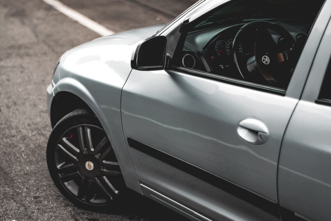 A detailed view of a silver car's side and interior in an urban environment, showcasing modern design.