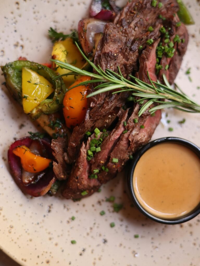 Delicious roasted lamb topped with chives beside grilled vegetables and a serving of gravy.