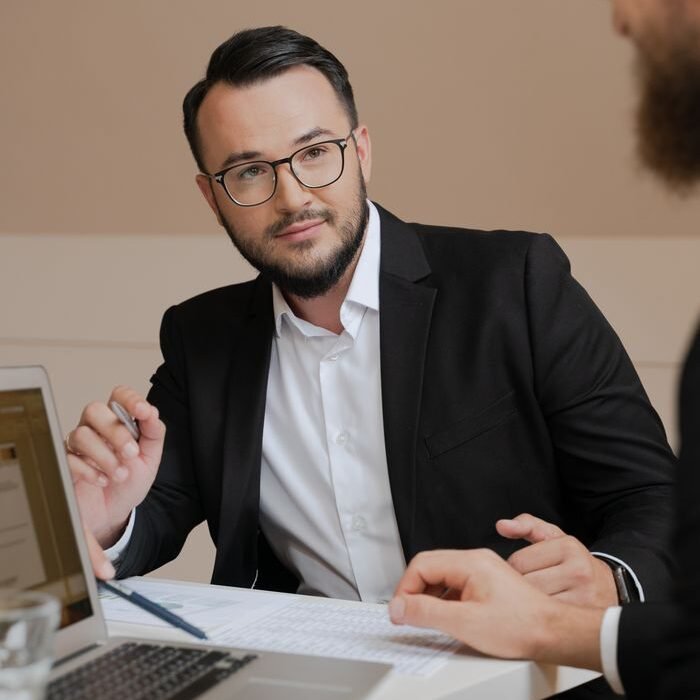 Two businessmen in a meeting discussing strategies with laptops and documents.